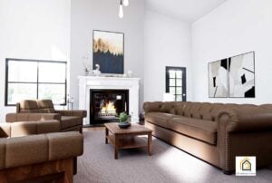 Warm and inviting living room inside The Arcadia barndominium with a fireplace, brown tufted furniture, and high ceilings.